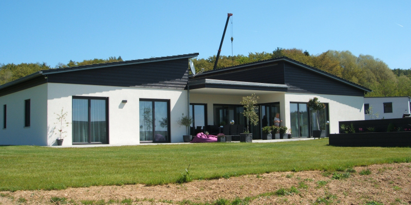 Moderner Bungalow mit Pultdach von der Wiesenseite, Baukran im Hintergrund