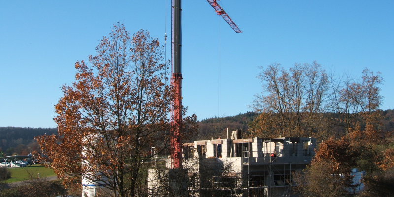 Einfamilienhaus-Rohbau mit rotem Baukran auf einem H&uuml;gel im Herbst
