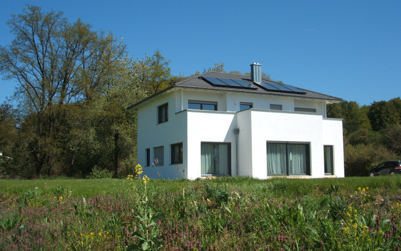 Freistehendes wei&szlig;es Einfamilienhaus mit Walmdach und Photovoltaik in einer Blumenwiese